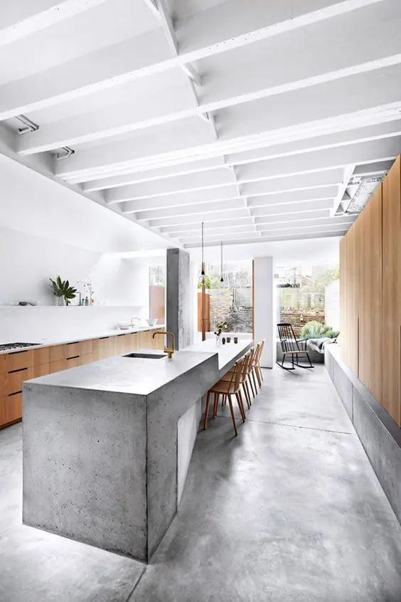 a sculptural and long concrete kitchen island features a dining space on one end