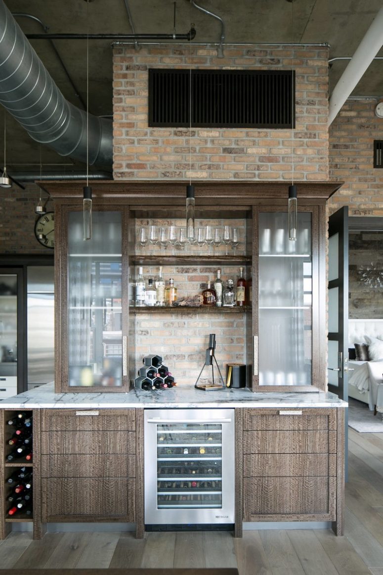 A home bar is done with the same cabinets attached to a brick wall and cool pendant lamps illuminate it