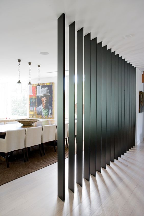a black wooden plank screen separates the dining room from the entryway and doesn't look bulky