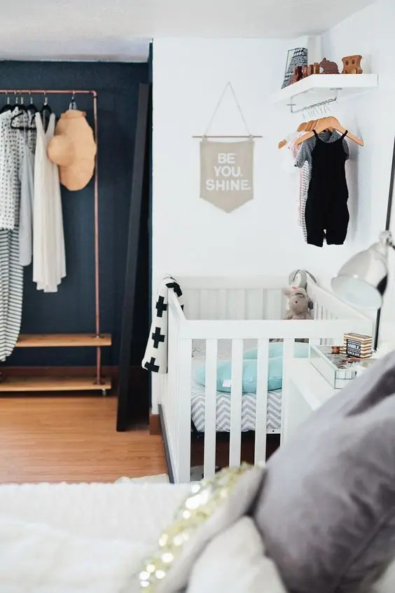 a chic master bedroom with an open closet and a baby's nook with a crib and a hanging closet over it