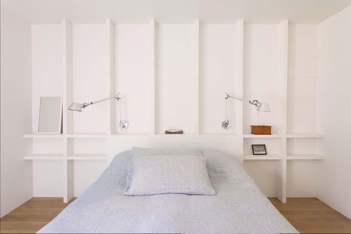 The master bedroom features white walls with shelves, a comfy bed and some sconces