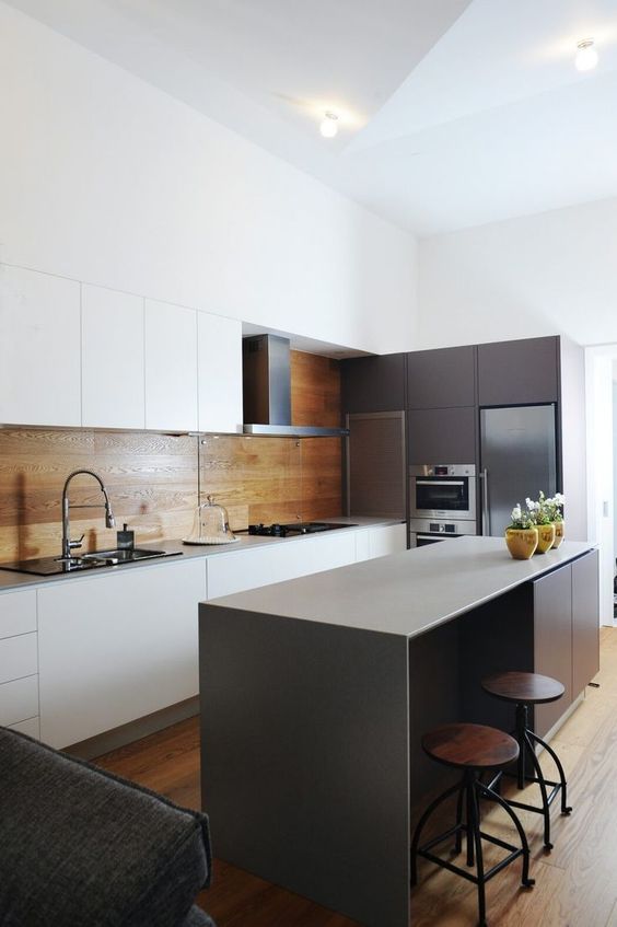 a minimalist kitchen with white sleek cabinets and a warm wood panel backsplash plus an additional glass screen in the cooker zone