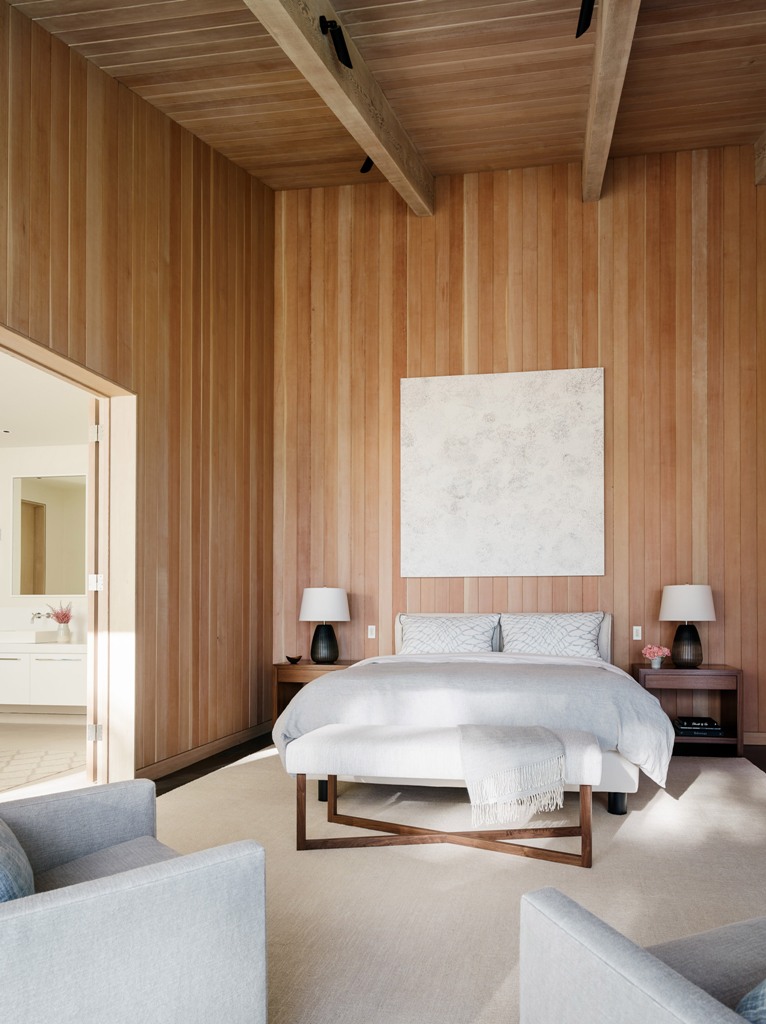 The master bedroom features comfortable contemporary furniture and much wood that clads the walls and a high ceiling
