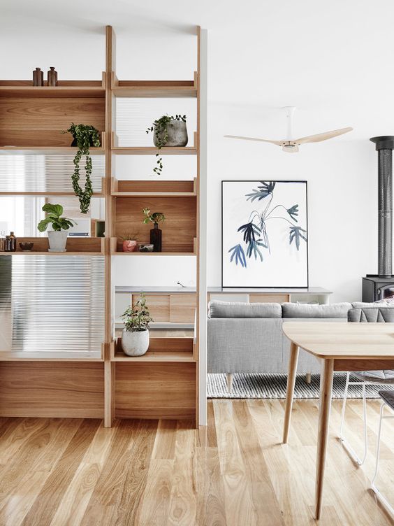a modern wooden shelving unit features open and box-shaped shelves with much potted greenery for separating from the dining room