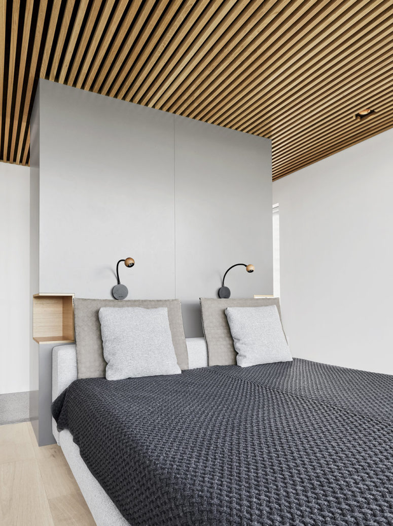 The master bedroom is done with an upholstered bed and a sleek grey headboard with built-in nightstands