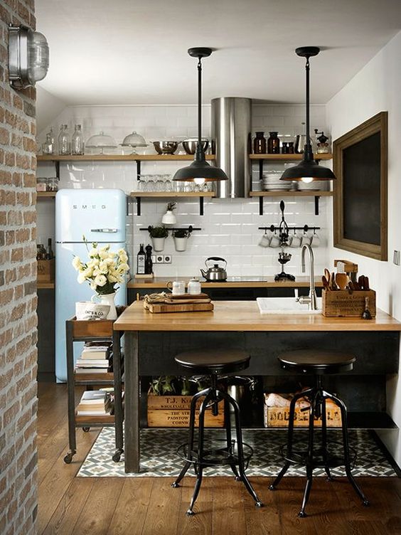 A kitchen island of blackened metal, with storage shelves and a light colored wooden tabletop plus a matching cart