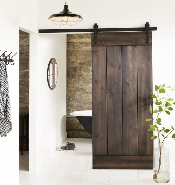 dark stained sliding barn door hides a small bathroom and stands out in a neutral space