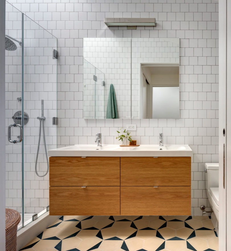 The bathroom is serene, with white tiles and a floating light colored wood vanity