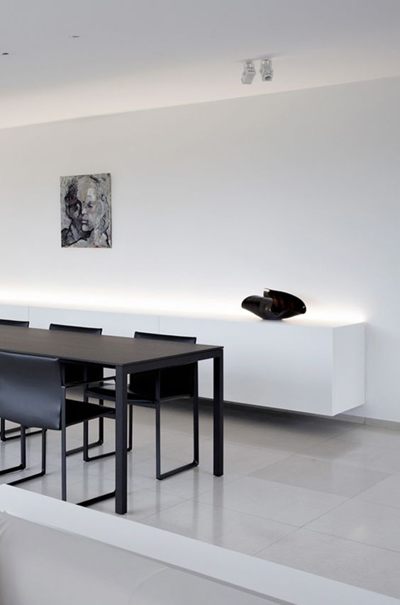 an ultra-minimalist space with a black dining set and a white floatign credenza with built-in lights