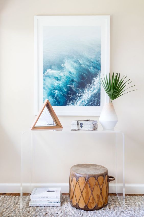a modern oasis entryway, with an acrylic console, an ocean artwork and a drum