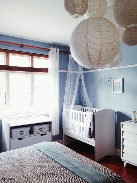 a peaceful blue master bedroom with a baby's corner with a crib and a changing table with baskets