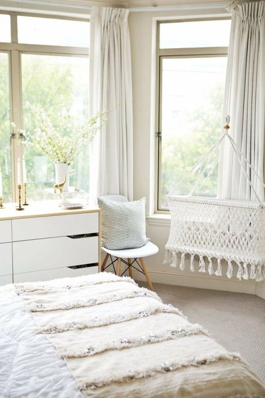 A peaceful light colored space with boho touches and a woven crib hanging by the window looks heavenly