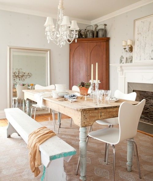 an antique table with whitewashed legs and modern white chairs and a bench for a softer vintage look