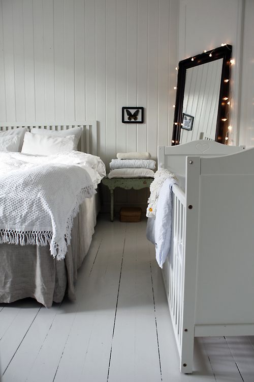 a peaceful shabby chic bedroom decorated in neutrals and a baby's crib by the wall