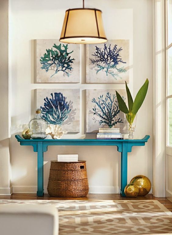 a coastal entryway with a turquoise console table, a basket and a gallery wall of watercolor sea artworks