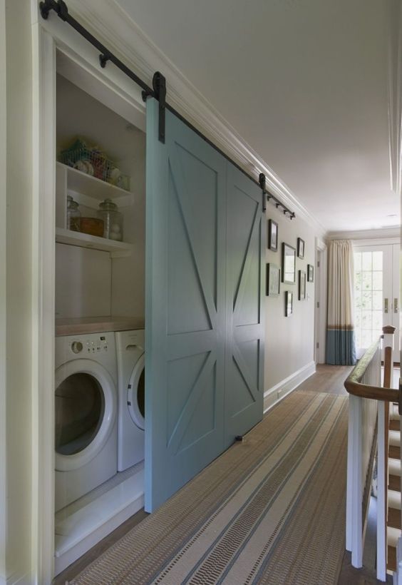 a large light blue barn door is used to hide a built-in laundry and keep the space neat