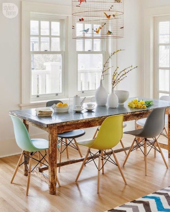 a vintage rustic table plus modern colorful chairs and a faux bird cage with colorful faux birds