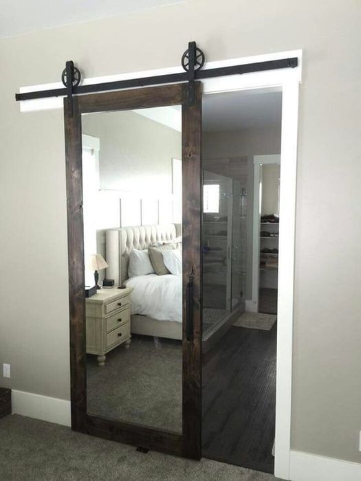 a dark stained barn door with a mirror insert hides a bathroom and a closet