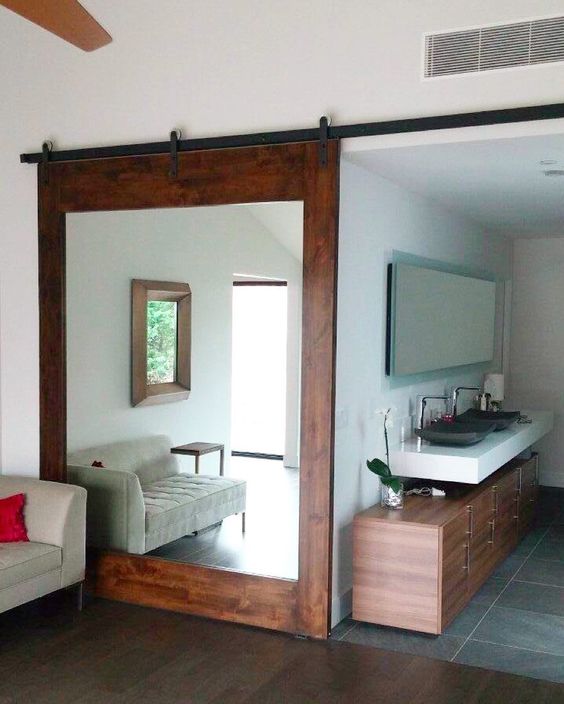 a rich-colored large barn door features a big mirror that doubles the living room space