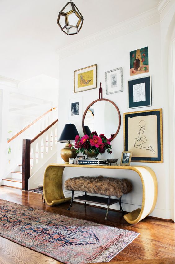 a stunning curved console, a fur ottoman and a gallery wall with various art and a mirror