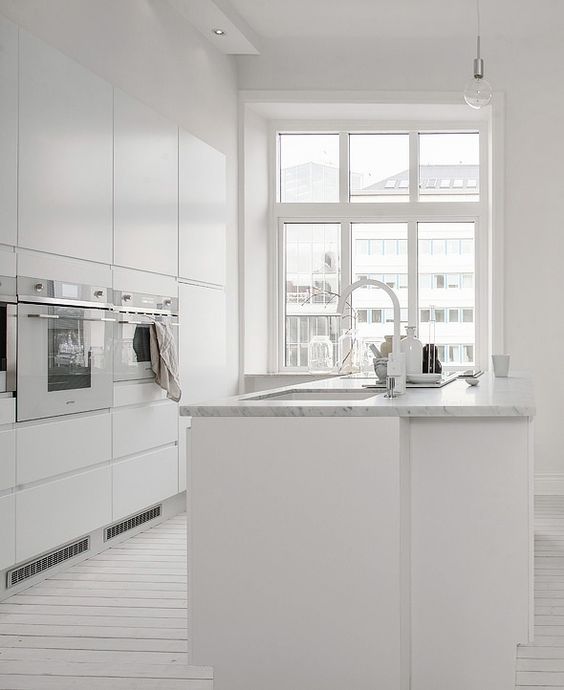 a whitewashed wooden floor and a white marble countertop are ideal to spruce up an all-white kitchen