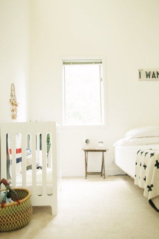 an uncluttered Scandinavian space with a crib, a basket and a bed with a small nightstand