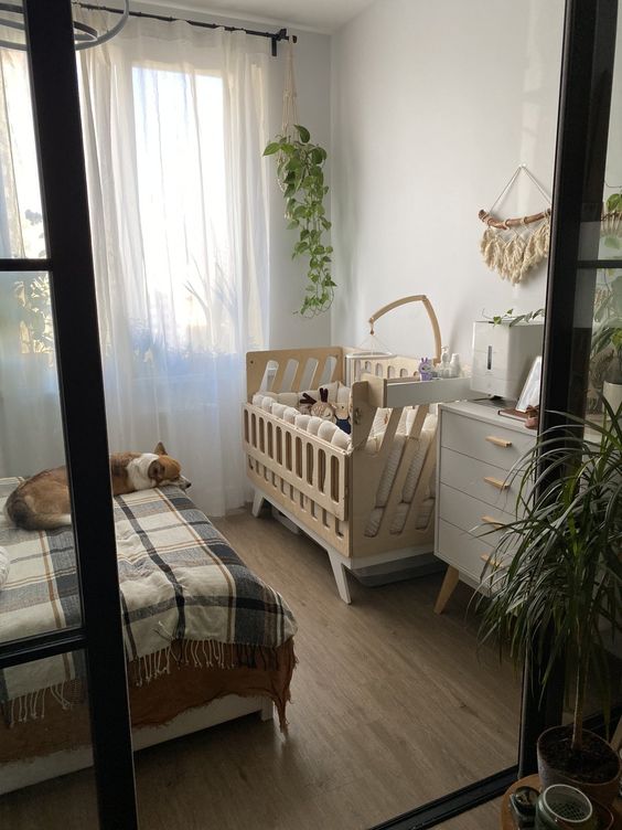 a Scandinavian boho bedroom with a large bed, a dresser with decor, an MDF crib, a macrame piece and some greenery