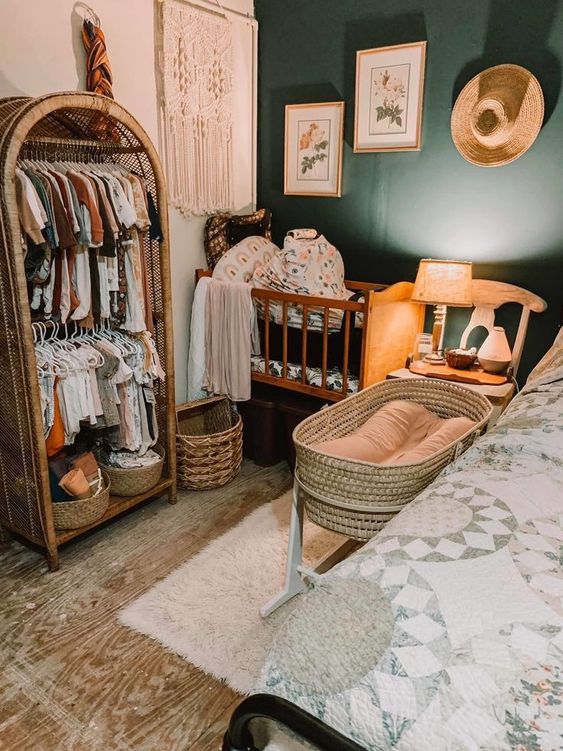 a boho bedroom with a dark green wall, a bed with a printed blanket, a makeshift baby's closet, a crub and some decor