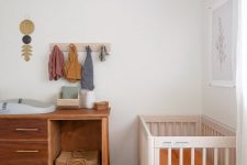 a boho master bedroom with a bed, a crib in the corner, a changing table of a dresser, some bright touches