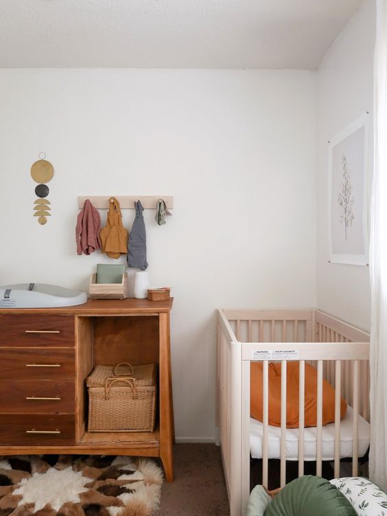 a boho master bedroom with a bed, a crib in the corner, a changing table of a dresser, some bright touches