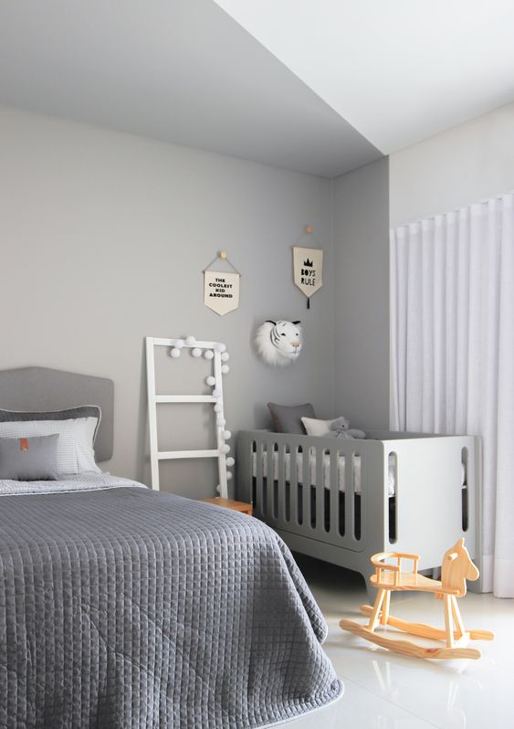 a grey master bedroom with a bed in the niche and grey bedding, a grey crib in the corner, a ladder, some toys and wall decor