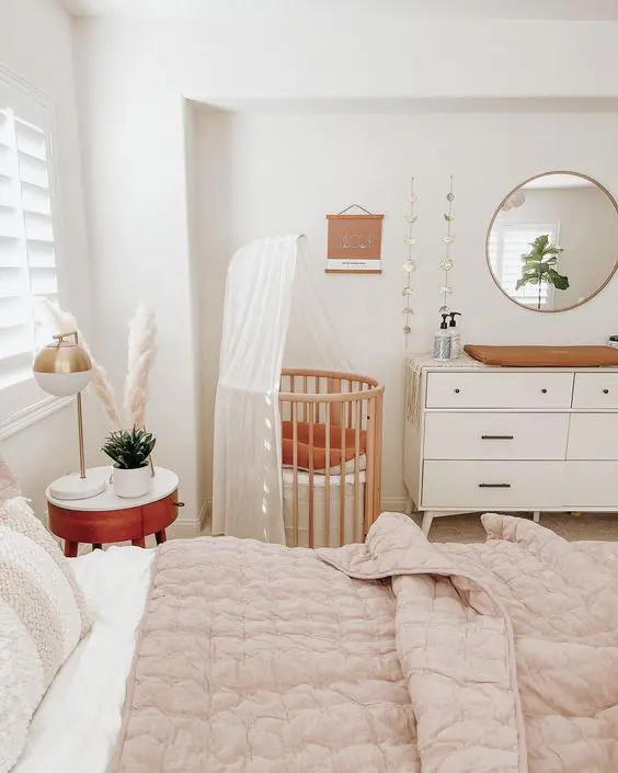 a lovely neutral boho bedroom with a bed and neutral bedding, a nigthstand with decor, a stained crib, a dresser as a changing table