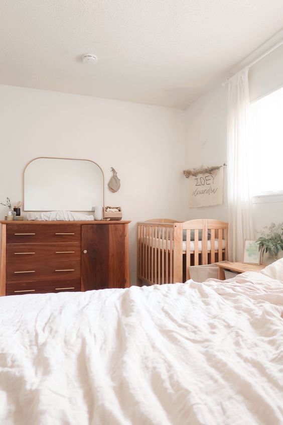 a minimal neutral bedroom with a stained dresser, a stained crib, a bed with neutral bedding and nightstands