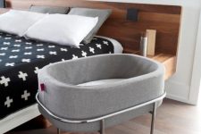 a modern bedroom with a stained bed, printed bedding, a crib on rockers is a cool idea for those who are expecting