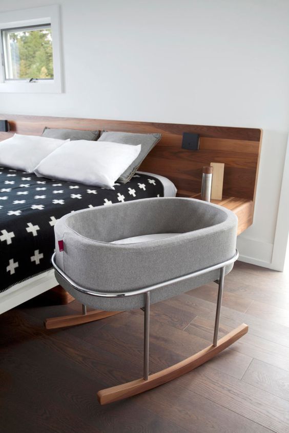 a modern bedroom with a stained bed, printed bedding, a crib on rockers is a cool idea for those who are expecting