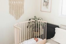 a modern boho bedroom with a bed and neutral bedding, a wooden crib, a stool with a potted plant and macrame