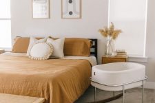 a modern boho bedroom with a black bed, rust bedding, a bassinet, a bench and some decor and art