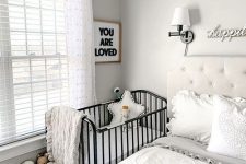 a modern light grey bedroom with a creamy bed and neutral bedding, a forged crib, a basket with toys and some decor