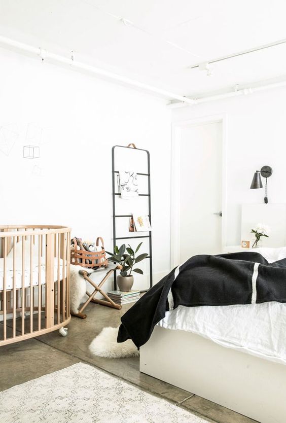 a modern neutral bedroom with a white bed, black and white bedding, black sconces, a ladder for storage, a crib on casters and a potted plant