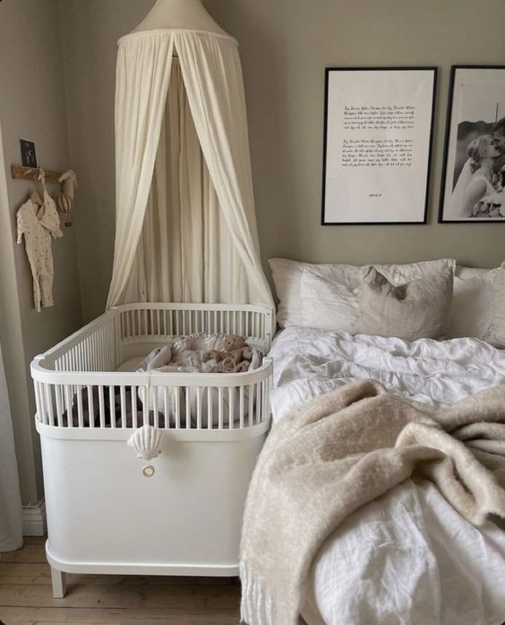 a neutral bedroom with grey walls, a bed with neutral bedding, a white crib with a canopy and some decor