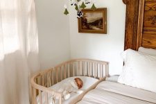 a neutral boho bedroom with a bed and a reclaimed wood headboard, neutral bedding, a stained crib and a mobile over it, some artwork