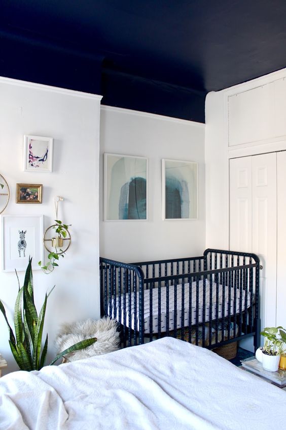 a neutral boho bedroom with a bed and neutral bedding, a black crib in the corner, a gallery wall and potted plants