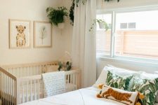 a tropical bedroom with a crib in the corner, a bed with neutral and printed bedding, a tassel chandelier and greenery
