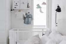 a white Scandinavian bedroom with white furniture, printed bedding, a crib in the corner, a mobile and some decor