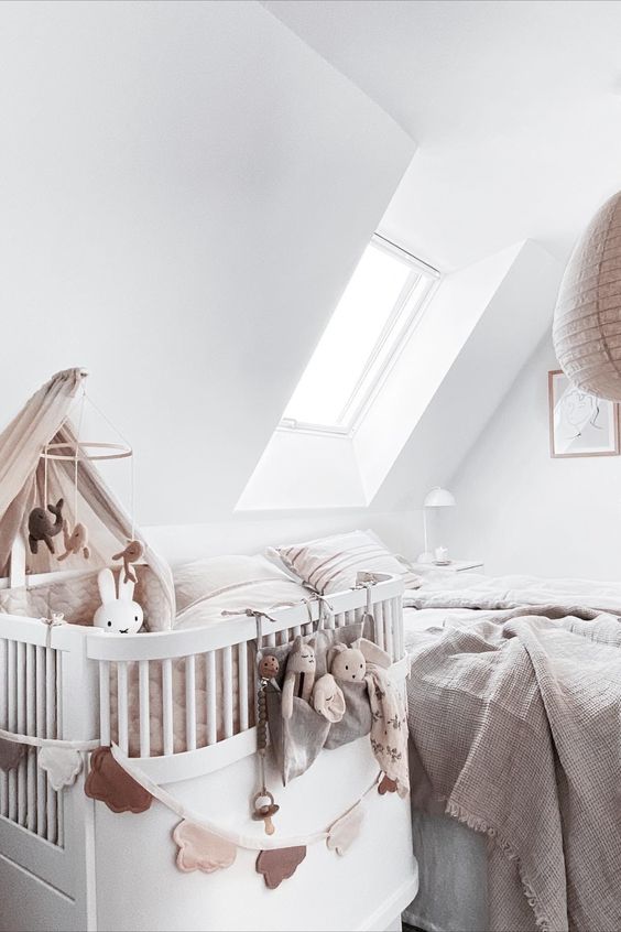a white bedroom with a skylight, a bed with neutral bedding, a white crib and toys and decor is cool