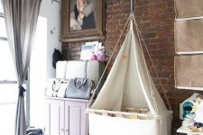 an eclectic bedroom with a brick wall, a pink cabinet, a chest, a bed, a suspended crib and makeshift baby’s closet