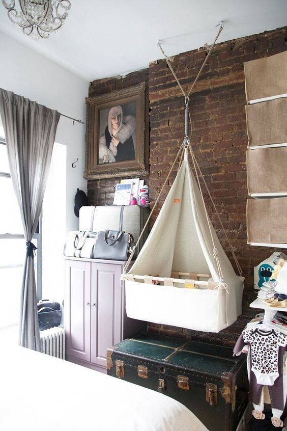 an eclectic bedroom with a brick wall, a pink cabinet, a chest, a bed, a suspended crib and makeshift baby's closet