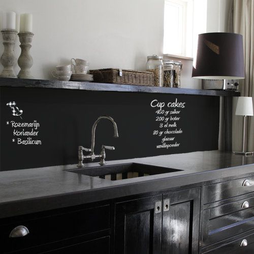 a black glossy kitchen with dark concrete countertops and a chalkboard backsplash to chalk on recipes and lists