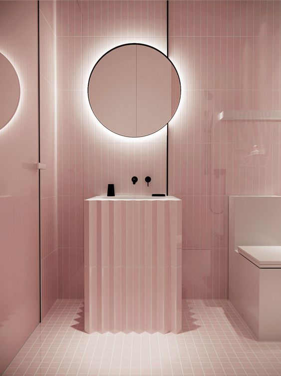 A minimalist light pink bathroom with black touches for depth and a mirror with built in lights