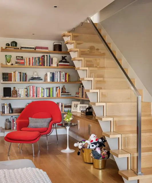 A reading nook with wall mounted shelves, cabinets and a bold red mid century modern chair